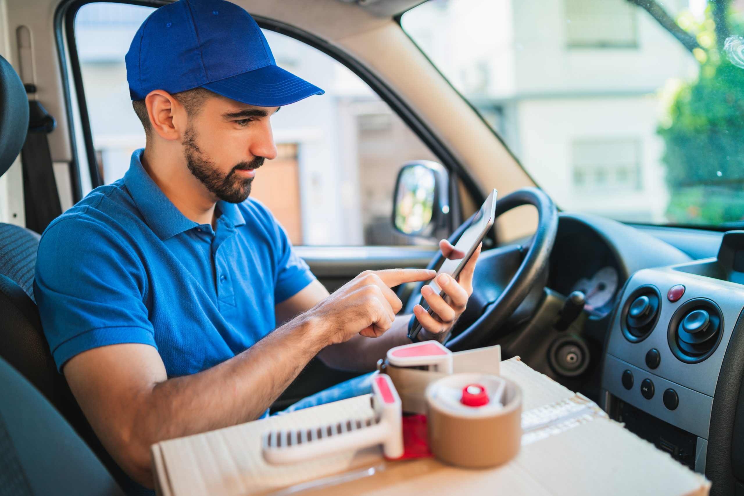 Portrait of a delivery man driver using digital tablet while sitting in van. Delivery service and shipping concept.