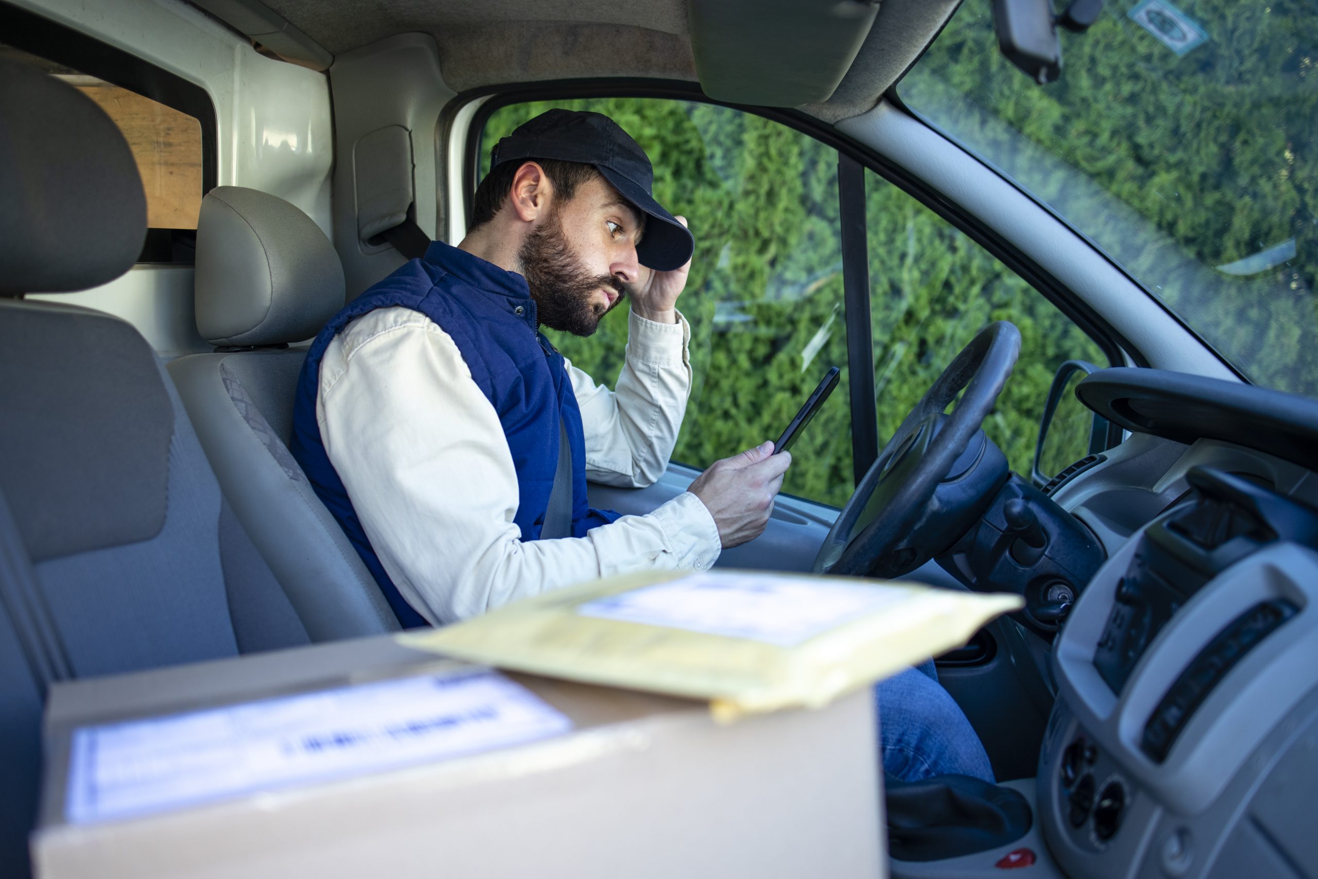 Delivery man in his van having difficulties finding the address to deliver parcel.