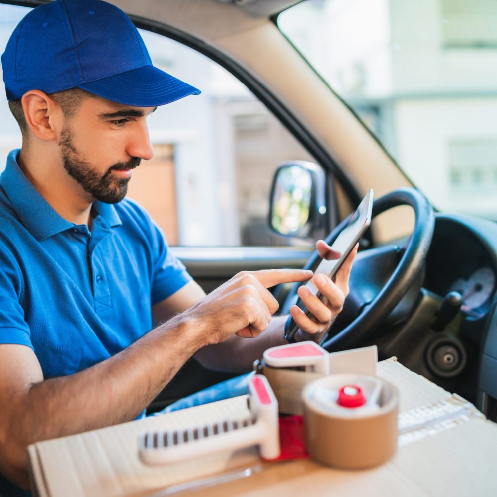 Portrait of a delivery man driver using digital tablet while sitting in van. Delivery service and shipping concept.